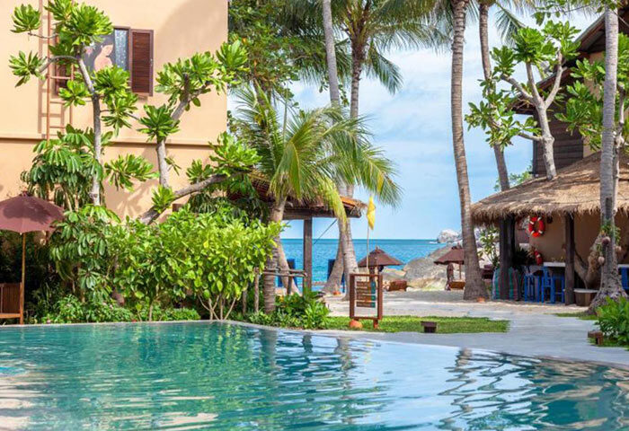 Buri Rasa Koh Phangan gay-friendly hotel pool view. Beachfront resort with palm trees, ocean, and thatched-roof bar. Best deals in Koh Phangan.