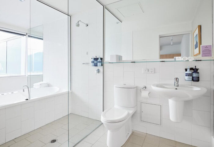 Saint Kilda Beach Hotel, Melbourne, gay honeymoon destination. White bathroom with tub, toilet, and sink. Modern design, ideal for gay couples.