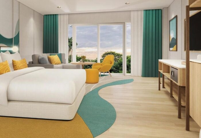 M Social Hotel Phuket room. Best gay honeymoon hotels this year. A spacious suite with bed, couch, chair, and balcony overlooking lush greenery.