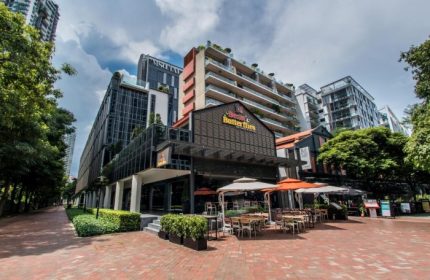 M Social Singapore, a top gay honeymoon hotel. Exterior view of the hotel, showcasing its modern architecture and outdoor dining area.