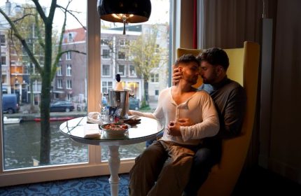 Gay couple embracing at Andaz Amsterdam Prinsengracht, a best gay hotel, with canal view, champagne, and snacks. Amsterdam gay travel.