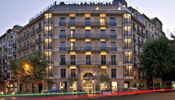 Axel Hotel Barcelona, a gay adults-only hotel in Eixample. Urban Spa. Facade of the building at dusk with light trails from passing cars.