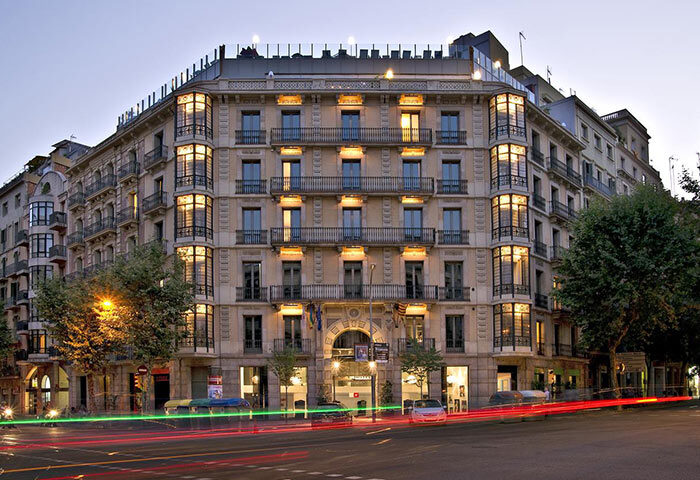 Axel Hotel Barcelona, a gay adults-only hotel in Eixample. Urban Spa. Facade of the building at dusk with light trails from passing cars.