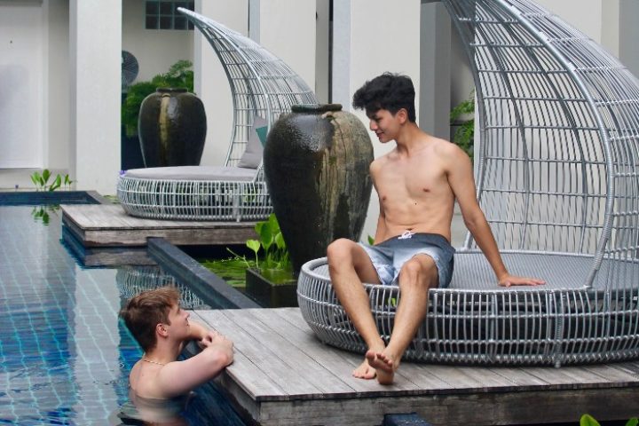 Gay honeymoon at Outrigger Surin Beach Resort, Phuket, Thailand. Two shirtless men relaxing by the pool in a luxury gay-friendly hotel.