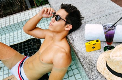 Gay man at M Social Singapore's rooftop pool. Enjoying a cocktail, he's relaxing at this best gay hotel in Singapore. Perfect for gay travel.