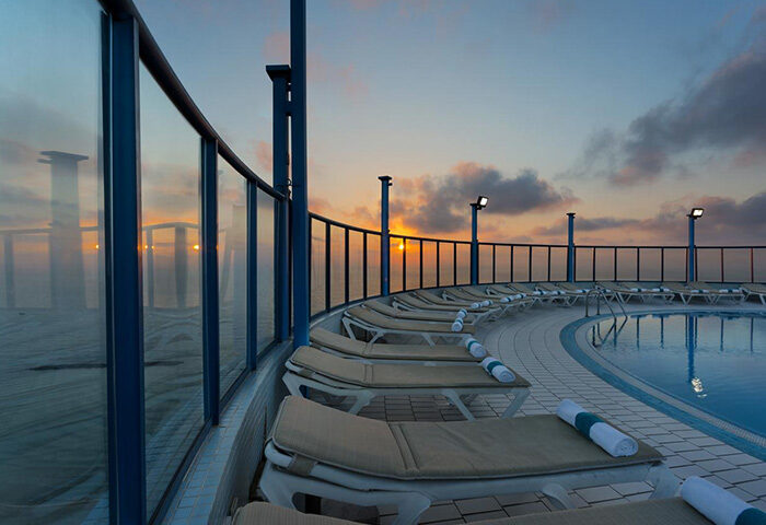 Isrotel Tower rooftop pool at sunset. Best gay hotel in Tel Aviv's gayborhood. Lounge chairs line the pool with a view of the city center.