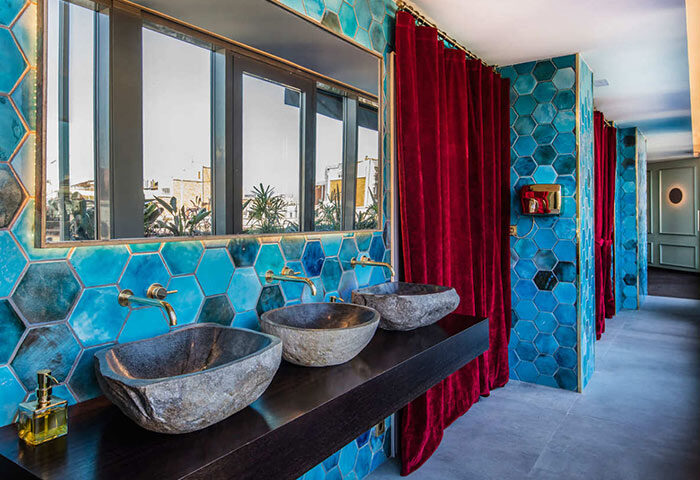 Bathroom at Axel Hotel Barcelona, a gay adults-only hotel. Stone sinks, blue hexagon tiles, and red velvet curtains create a stylish urban spa.
