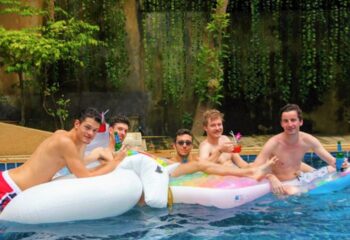 Gay men at Alpha Gay Resort & Spa, Koh Samui. Travelers relax in a pool with drinks on floats. Best gay hotel to meet other gay travelers.