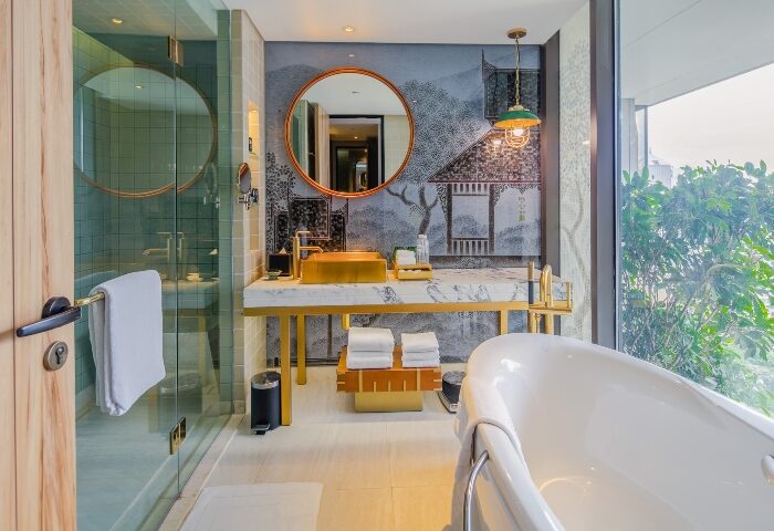 Hotel Indigo Bangkok Wireless Road bathroom. Gold sink, marble counter, soaking tub, and city view. Best gay hotels Bangkok on social media.