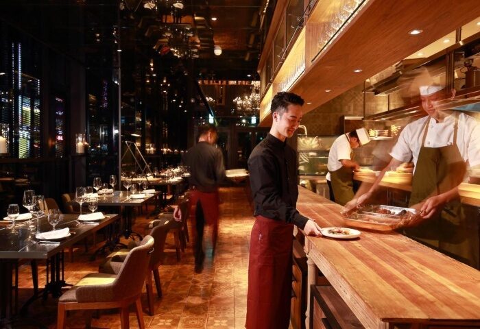 Hotel Proverbs Taipei restaurant. Chefs prepare food in the open kitchen. Tables are set for diners. Gay-friendly hotel near Taipei nightlife.