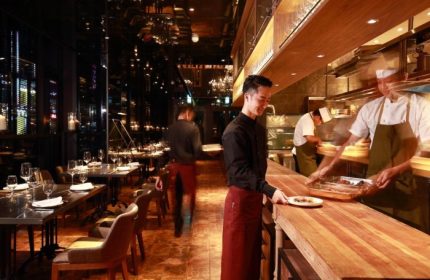 Hotel Proverbs Taipei restaurant. Chefs prepare food in the open kitchen. Tables are set for diners. Gay-friendly hotel near Taipei nightlife.