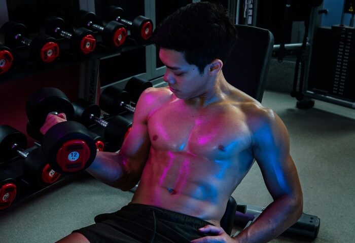 Man at M Social Singapore gym. Best gay hotels location near gay saunas. Shirtless man works out with dumbbells. Fitness.