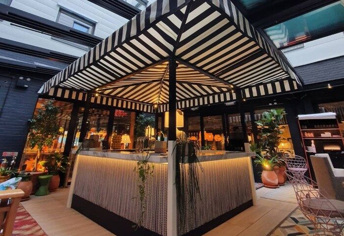 Stylish bar area at Mama Shelter London Shoreditch, one of the best gay-friendly hotels in London. Features a striped awning and lush plants.