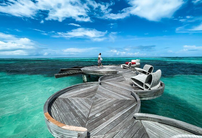 LUX* South Ari Atoll, Maldives water villas. Man on a wooden deck above turquoise water. Best gay hotels offer luxury and privacy.