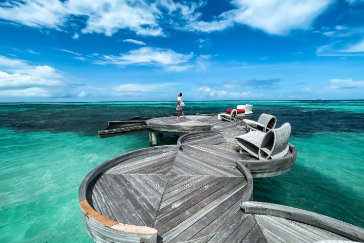 LUX* South Ari Atoll, Maldives water villas. Man on a wooden deck above turquoise water. Best gay hotels offer luxury and privacy.