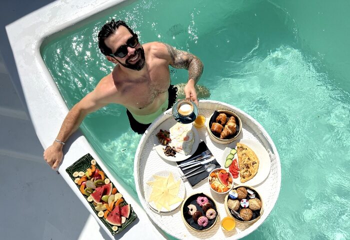 Gay man enjoying breakfast in a pool at Akkadian Gay Only Hotel, Mykonos. Best gay hotels on Instagram. Gay travel.