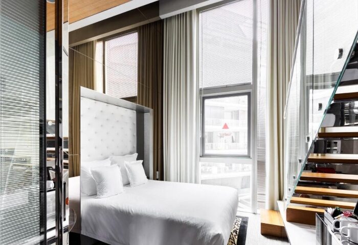 M Social Singapore loft room. Modern hotel near gay bars in Singapore. White bedding, large windows, and staircase. Best gay hotels for gay travelers.
