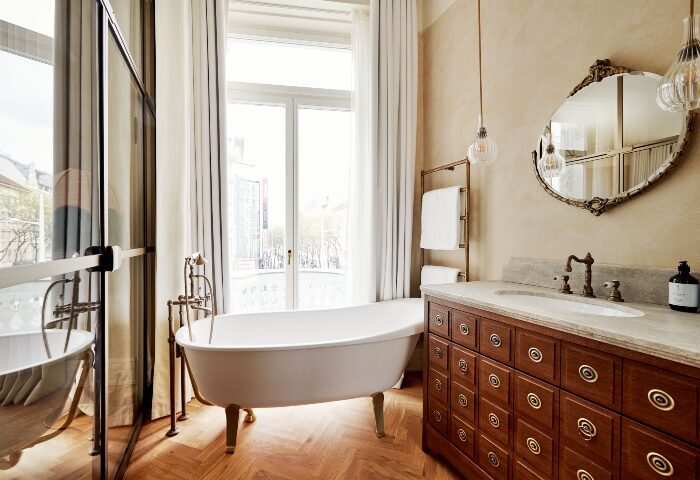 Hotel Motto Vienna bathroom. Clawfoot tub, herringbone floor, vanity with marble top, and ornate mirror. Best gay hotels for TikTok.