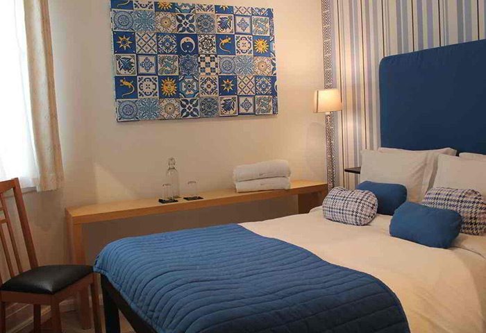 My Rainbow Rooms gay men's guest house room. Blue themed decor, bed with pillows, wall art, and chair. Best gay hotel in Lisbon city center.