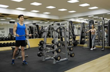 Gym at voco Orchard Singapore, an IHG Hotel. Gay wellness luxury hotel. Man lifting weights, woman on machine. Best gym in Singapore.