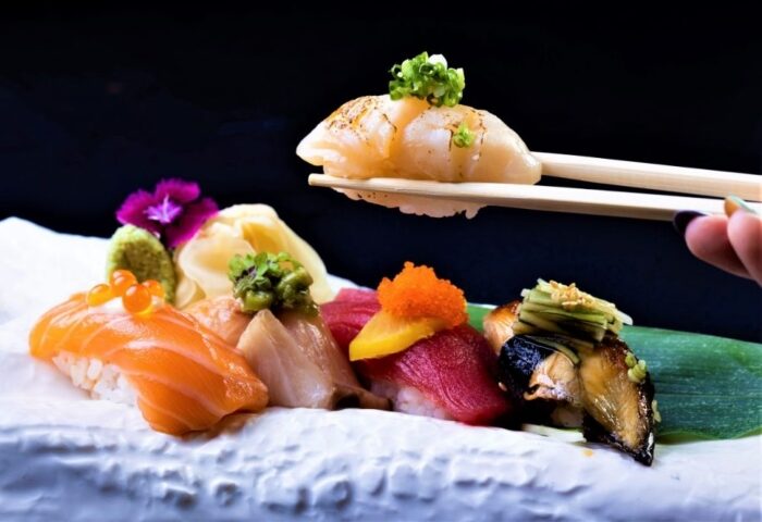 Soshi sushi at SO Bangkok Hotel, a perfect start to your gay night out! Best Japanese food in Bangkok's gayborhood. Chopsticks holding scallop.
