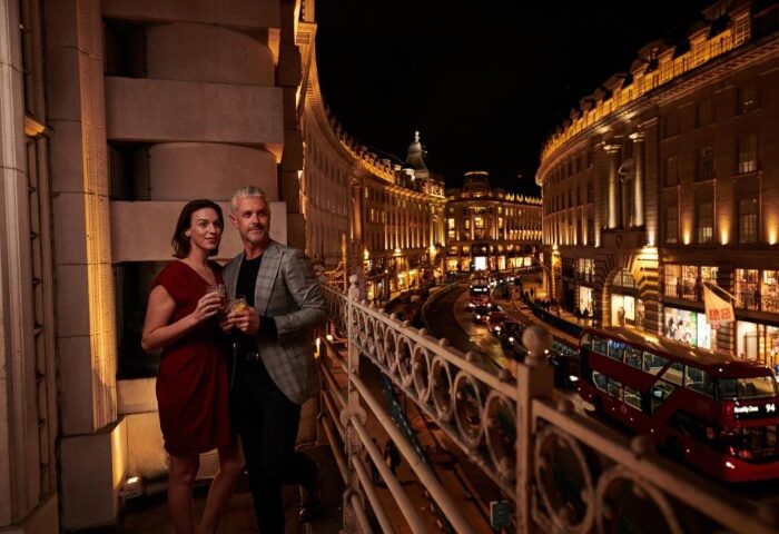 LGBTQ honeymoon at The Dilly, London. Couple on a balcony overlooking Regent Street at night. Best gay hotels in Soho, London.