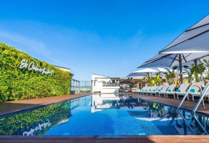 Sofitel Barcelona Skipper rooftop pool. Luxury gay hotel near Barcelona's Mar Bella gay beach. Loungers, umbrellas, and blue sky.