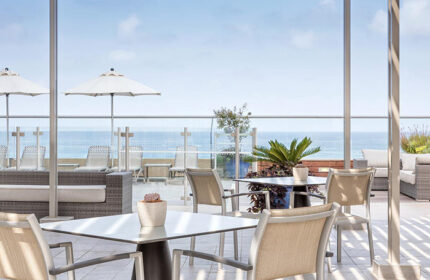 Sheraton Tel Aviv Hotel's luxury update. Ocean view from the terrace with tables, chairs, and parasols near Hilton Gay Beach.