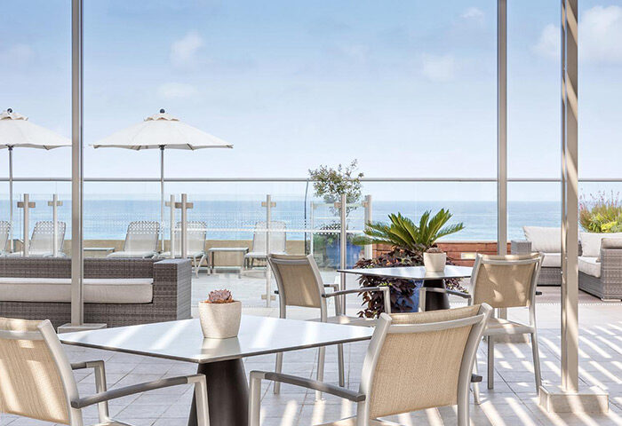 Sheraton Tel Aviv Hotel's luxury update. Ocean view from the terrace with tables, chairs, and parasols near Hilton Gay Beach.