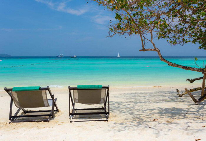 Koh Phi Phi gay honeymoon: Private beachfront with lounge chairs, turquoise water, and a sailboat. Perfect for a romantic gay getaway.