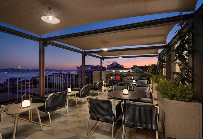 Bairro Alto Hotel rooftop restaurant at dusk. Romantic honeymoon hotel near gay nightlife, Lisbon. Tables, chairs, city view.
