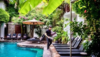 Rambutan Resort Siem Reap pool area. Best stay for gay solo travelers in Siem Reap City Center. Lush greenery, lounge chairs, and a man with pillows.