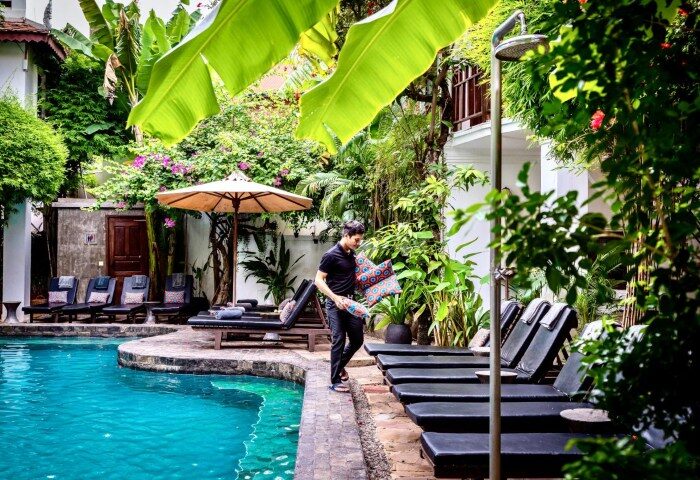 Rambutan Resort Siem Reap pool area. Best stay for gay solo travelers in Siem Reap City Center. Lush greenery, lounge chairs, and a man with pillows.