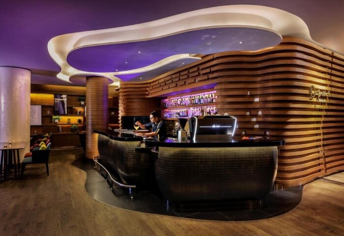 Stylish bar at voco Orchard Singapore, an IHG Hotel. Best Sunday brunch spot for gay travelers. Modern design, wooden accents, and a bartender crafting cocktails.