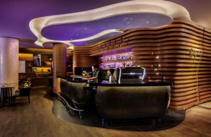 Stylish bar at voco Orchard Singapore, an IHG Hotel. Best Sunday brunch spot for gay travelers. Modern design, wooden accents, and a bartender crafting cocktails.