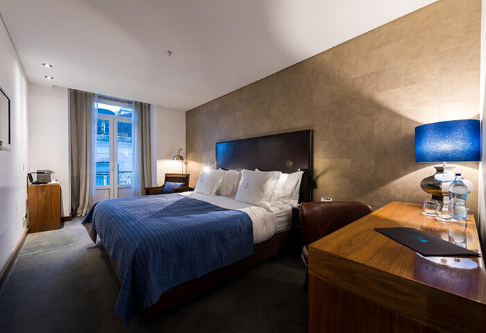 Lisboa Carmo Hotel room, honeymoon ideas in Lisbon city center gayborhood. Bed with blue cover, desk, and balcony. Best update hotel.