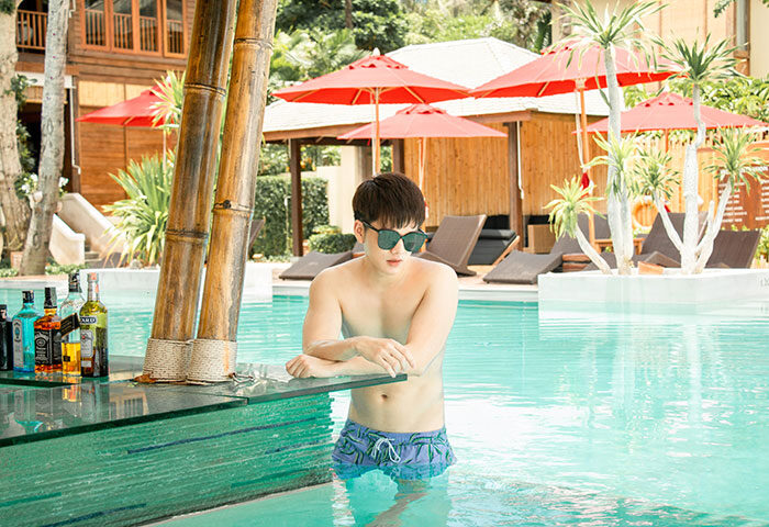 Gay couple's luxury beach vacation at Anantara Rasananda Koh Phangan Villas. Man in pool bar, tropical paradise, sun, drinks, relaxation.