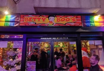 Betty Boo's Gay Bar in Benidorm. Entrance view with people inside, rainbow flag, and Christmas decorations. Gay travel advice.
