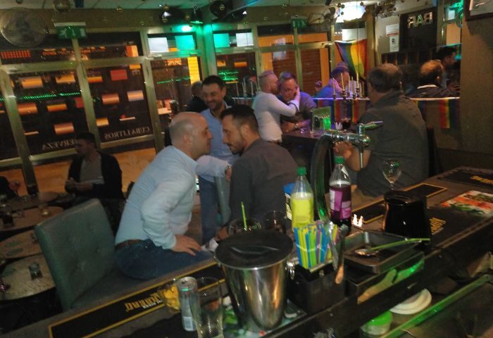 Betty Boo's gay bar in Benidorm. Men socializing at the bar, rainbow flag in the background. Gay travel destination, nightlife.