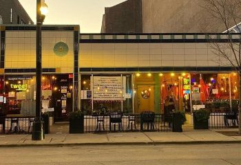 Big Chicks, a gay bar in Chicago. Exterior view of the bar with outdoor seating and warm lighting. A popular spot for gay men.