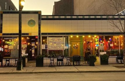 Big Chicks, a gay bar in Chicago. Exterior view of the bar with outdoor seating and warm lighting. A popular spot for gay men.