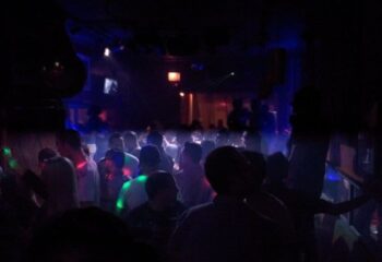 Crowded gay bar in Chicago. People dancing under blue & green lights. Big Chicks is a popular LGBTQ+ venue for gay men's travel.