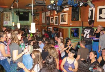 Crowded Big Chicks gay bar in Chicago. People socializing under warm lighting. Diverse crowd, lively atmosphere. Gay travel destination.