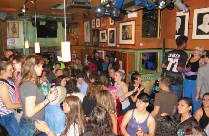 Crowded Big Chicks gay bar in Chicago. People socializing under warm lighting. Diverse crowd, lively atmosphere. Gay travel destination.