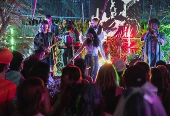 Band performs at BirdCage Club, Hanoi. Singer with angel wings on stage, musicians, & crowd. Gay travel in Vietnam nightlife scene.