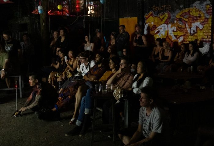 BirdCage Club Hanoi scene. Diverse crowd watching a performance. Graffiti art backdrop. Gay travel nightlife experience.