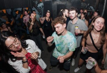 BirdCage Club Hanoi: Gay men dance, drink, and socialize in a crowded nightclub. Graffiti art adorns the walls. Nightlife scene.