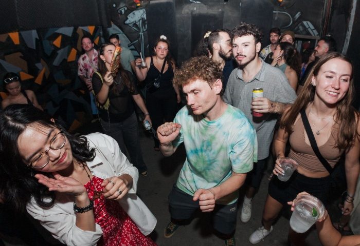 BirdCage Club Hanoi: Gay men dance, drink, and socialize in a crowded nightclub. Graffiti art adorns the walls. Nightlife scene.