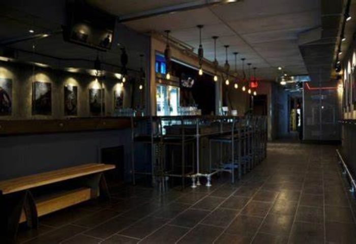 Interior of Black Eagle cruising bar in Toronto. Dark, industrial-chic decor, bar stools, bench, and tiled floor. Gay travel destination.