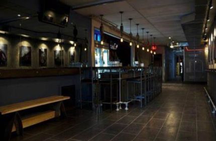 Interior of Black Eagle cruising bar in Toronto. Dark, industrial-chic decor, bar stools, bench, and tiled floor. Gay travel destination.